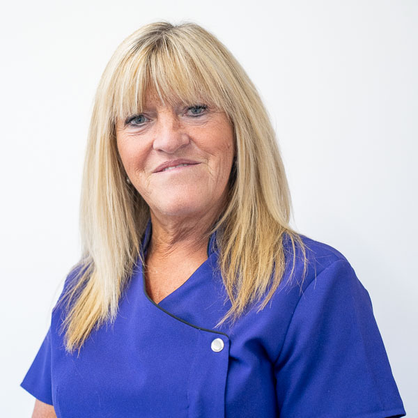 A woman with long blonde hair wearing a blue buttoned uniform smiles at the camera against a plain white background.