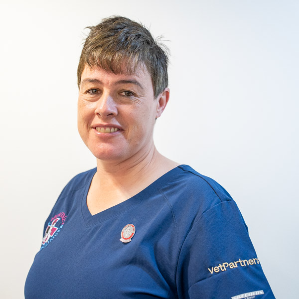 Person smiling, wearing a blue shirt with logos on it, standing against a plain light background.