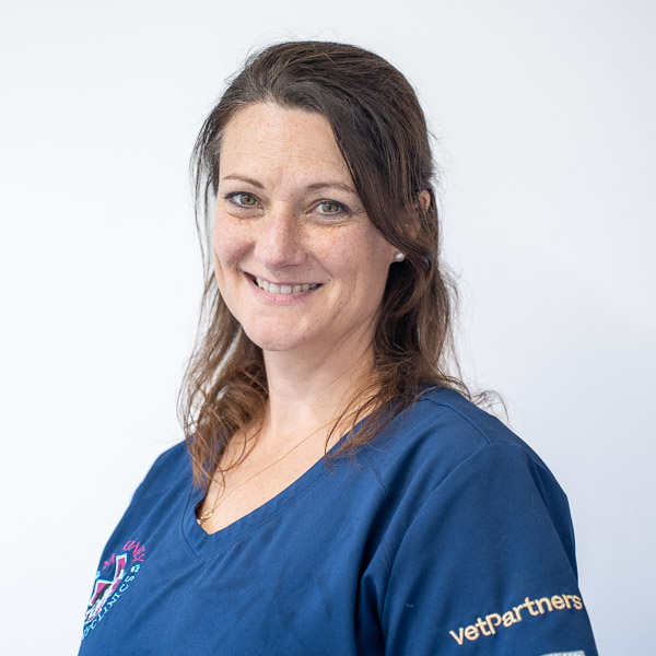 A woman with long brown hair smiling, wearing a navy blue top with embroidered logos. The background is plain white.